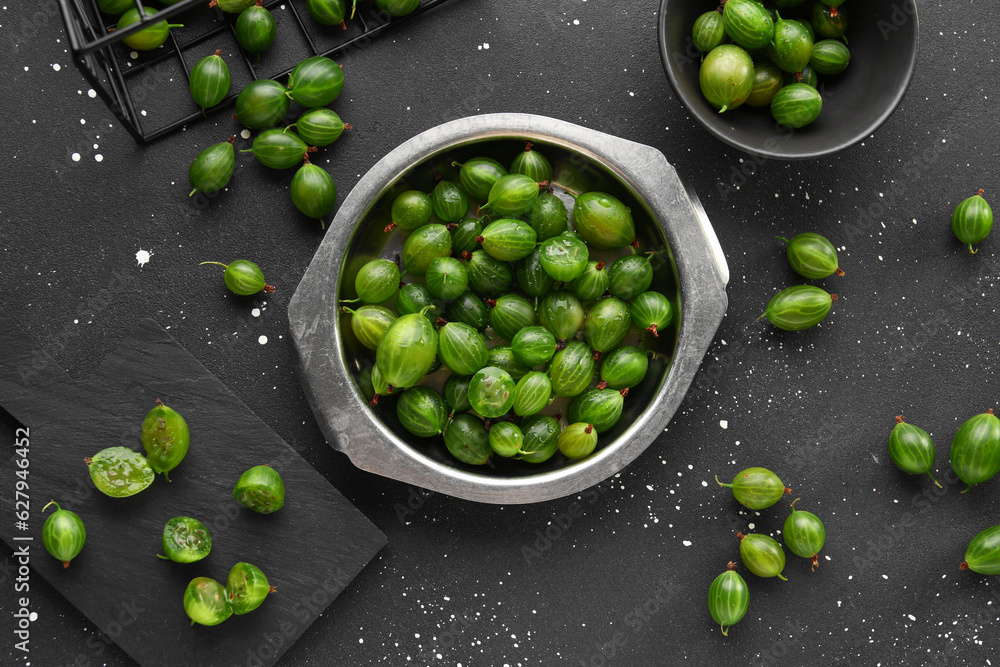 Metal plate and bowl with fresh gooseberries on black background