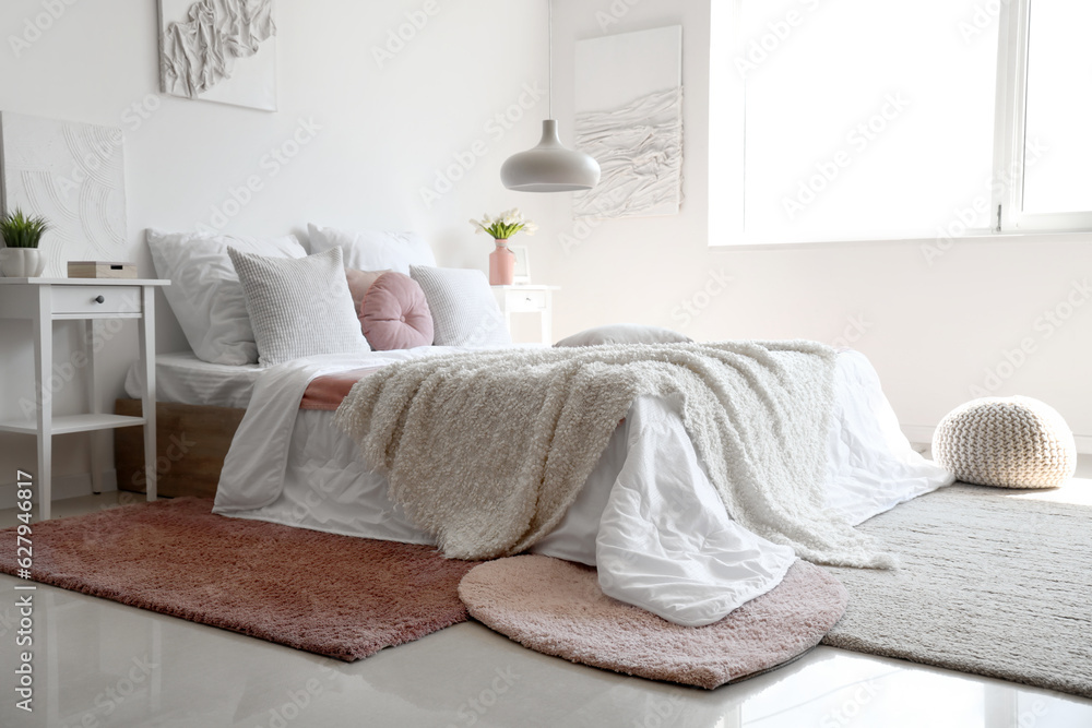 Cozy bed with white blanket and pillows in interior of light bedroom