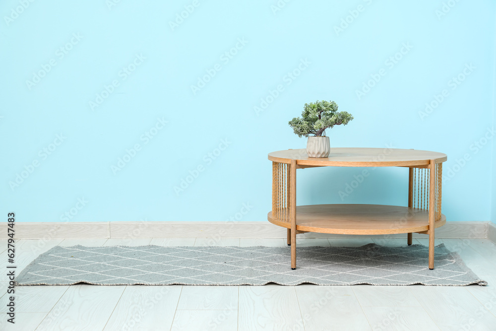 Wooden table with bonsai tree and stylish rug near blue wall