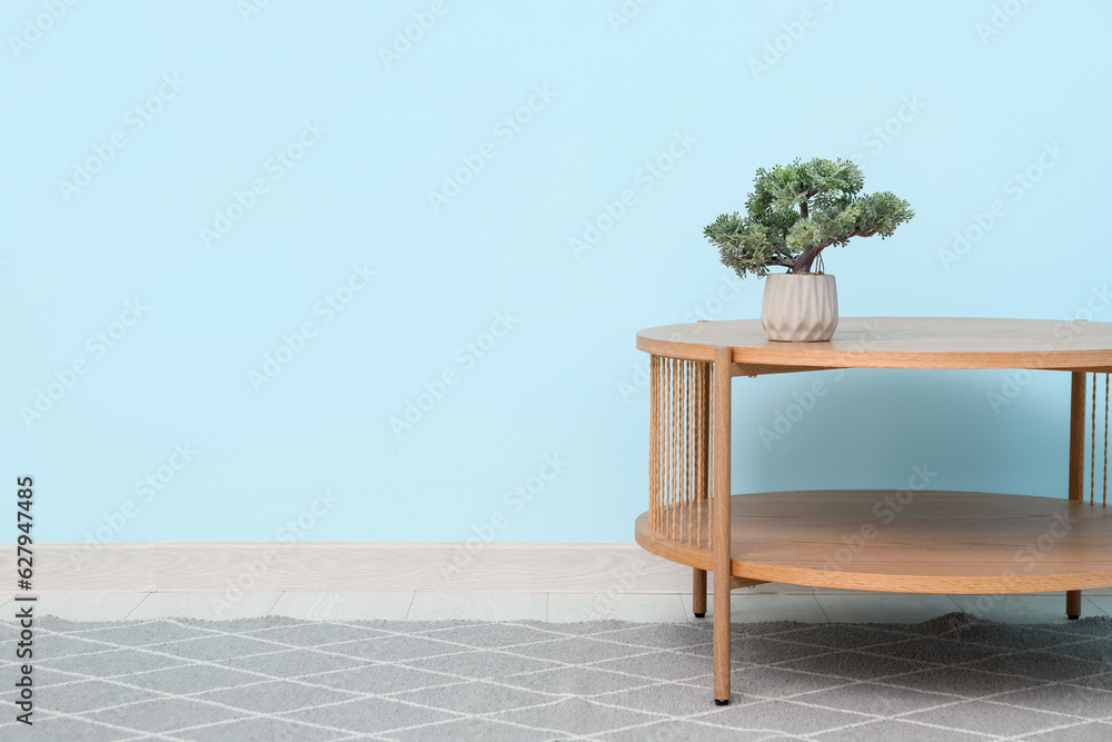 Wooden table with bonsai tree and stylish rug near blue wall