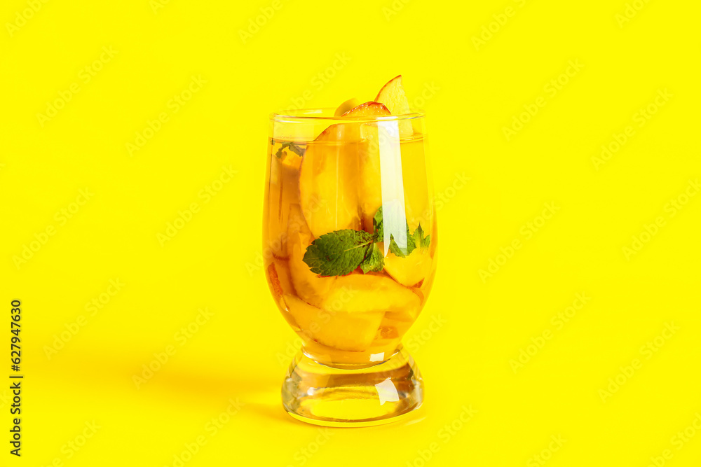 Glass of fresh peach lemonade with mint on yellow background