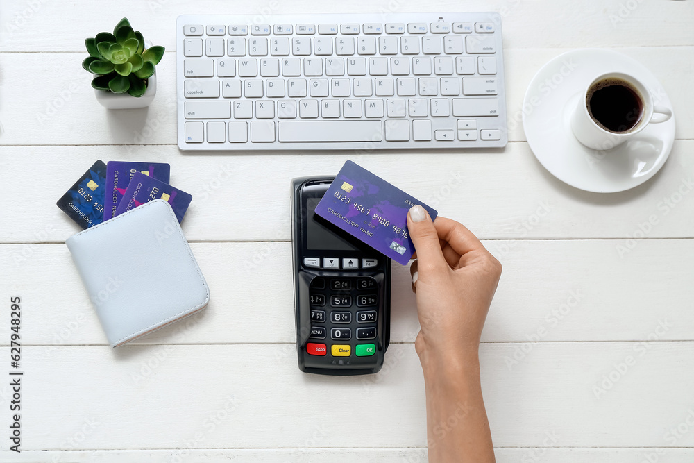 Female hand with payment terminal, keyboard and credit cards on white wooden background