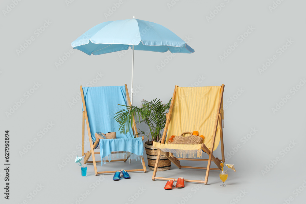 Deckchairs, beach accessories and glasses of cocktail grey background