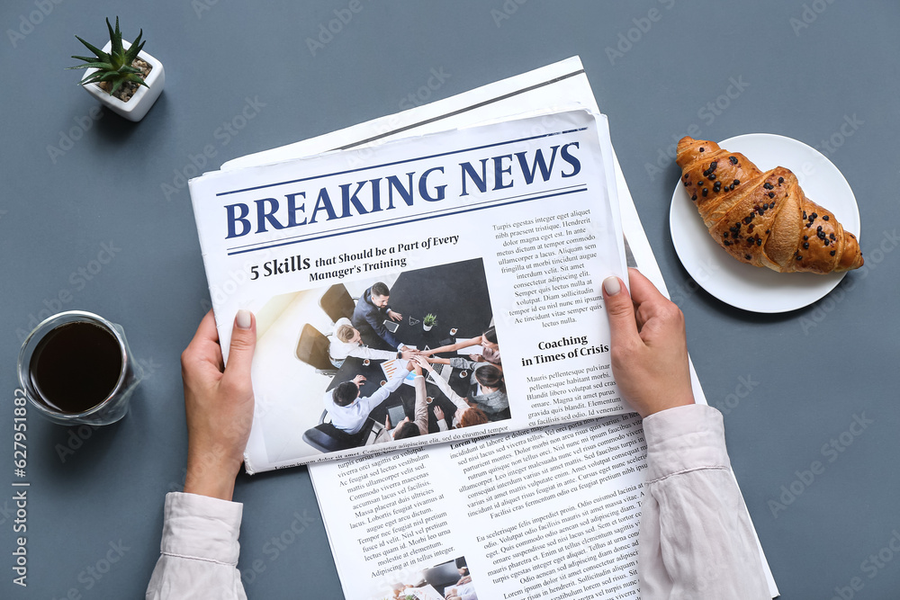 Woman reading newspaper with coffee and croissant on grey background