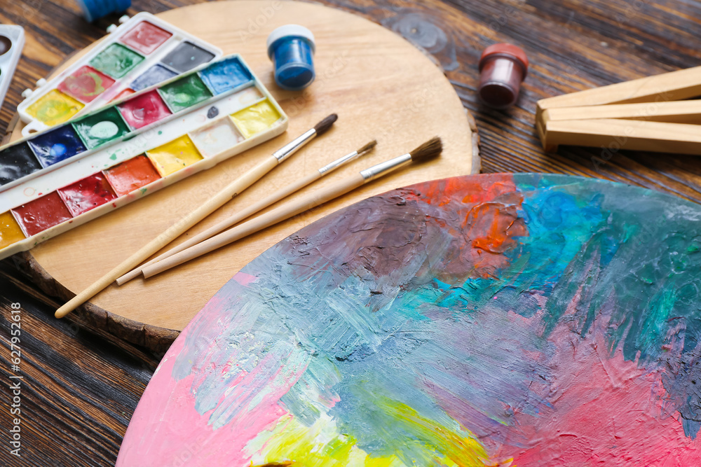 Palette with watercolor paints and brushes on wooden table