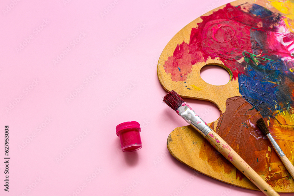 Brushes and palette with paints on pink background, closeup