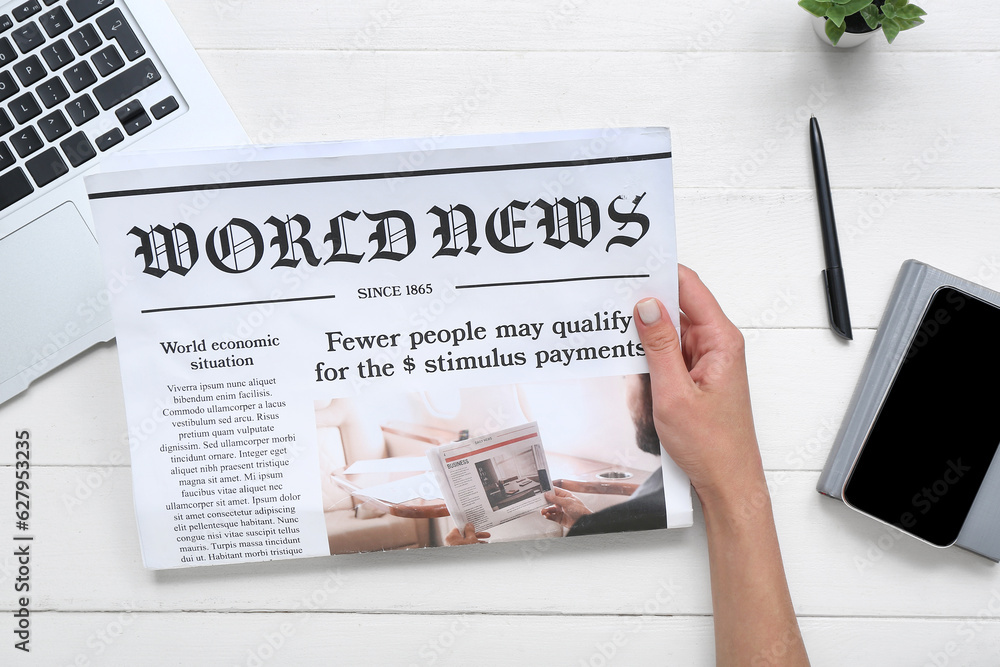 Woman reading newspaper at workplace with mobile phone on white wooden background