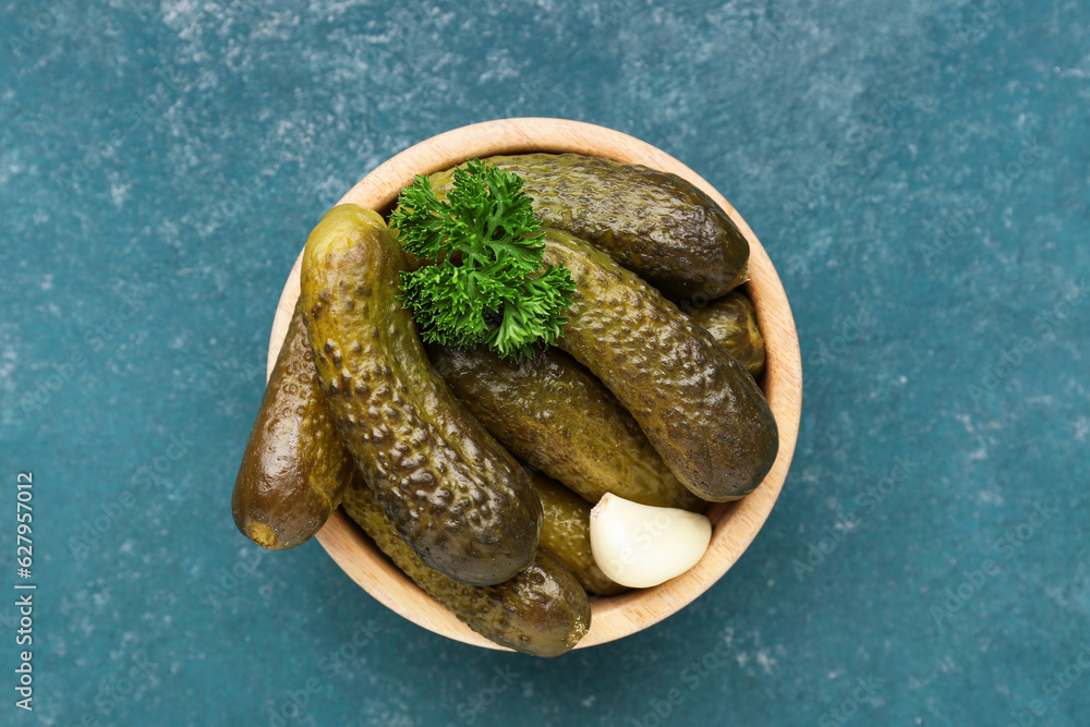 Wooden bowl with pickled cucumbers, parsley and garlic on blue background