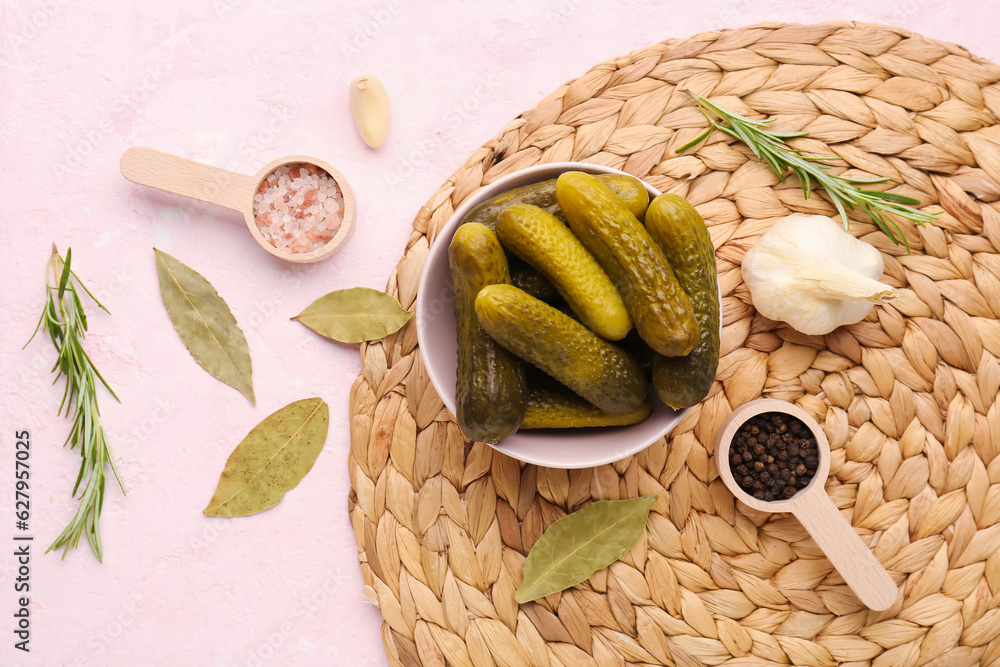 Bowl with pickled cucumbers and different spices on pink background