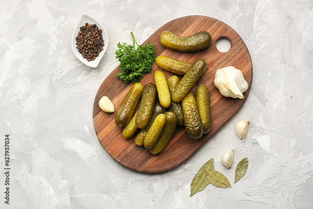 Wooden board with pickled cucumbers and different spices on grey background