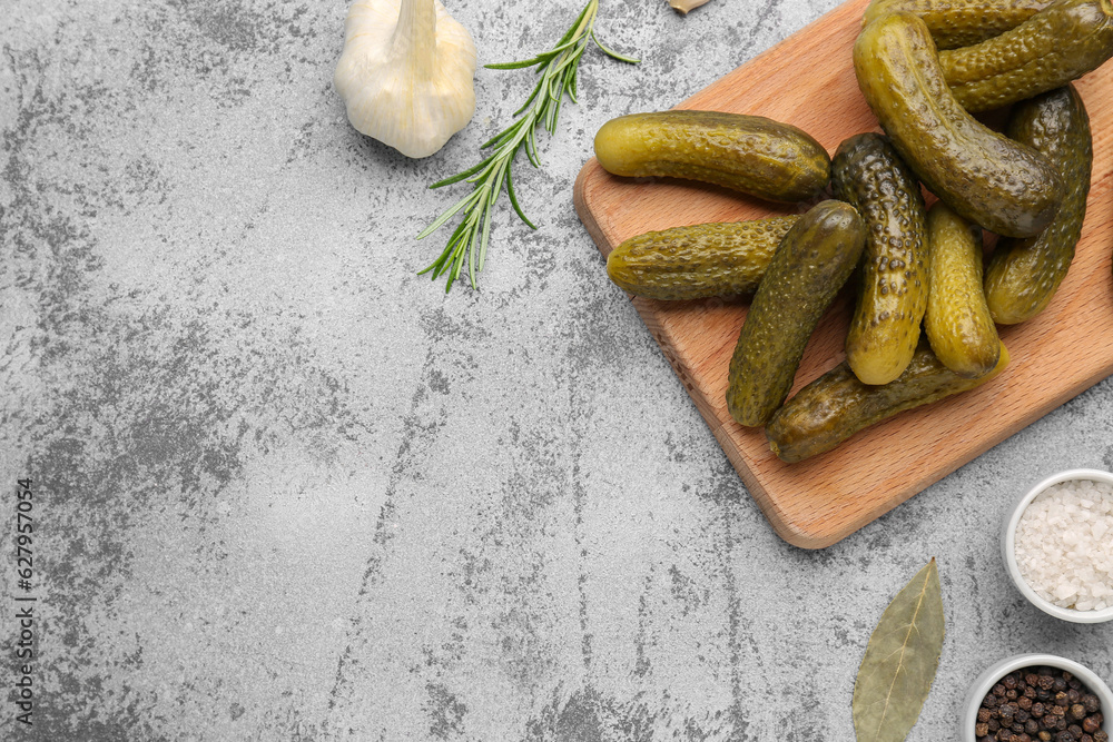 Wooden board with pickled cucumbers and different spices on blue background