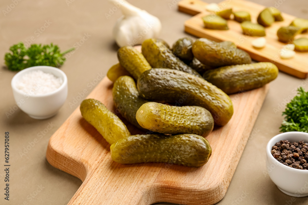 Wooden board with pickled cucumbers and different spices on brown background