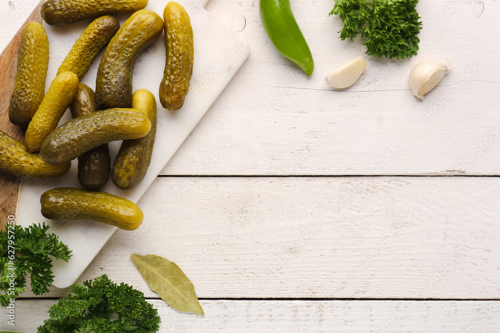 Board with pickled cucumbers and different spices on white wooden background