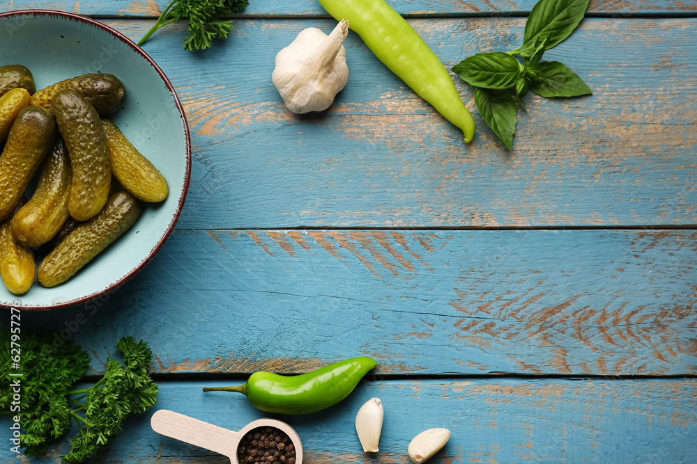 Bowl with pickled cucumbers and different spices on blue wooden background