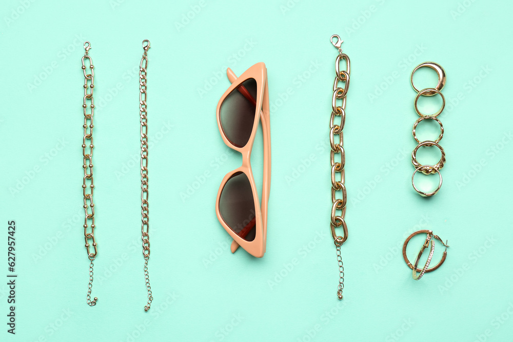 Stylish sunglasses with beautiful jewellery on turquoise background