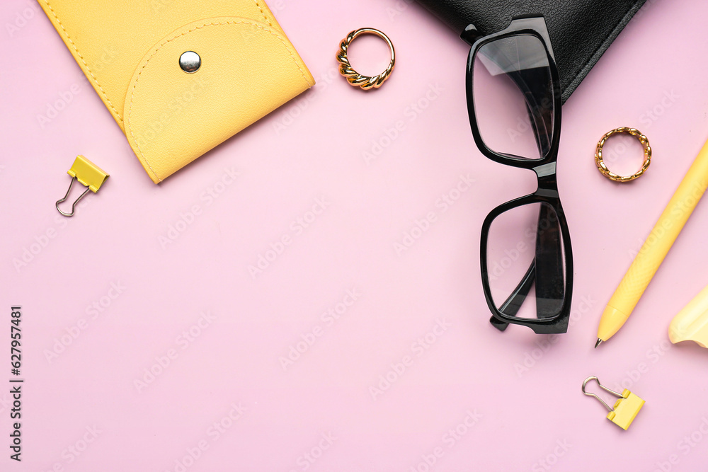 Stylish eyeglasses with stationery supplies and rings on pink background