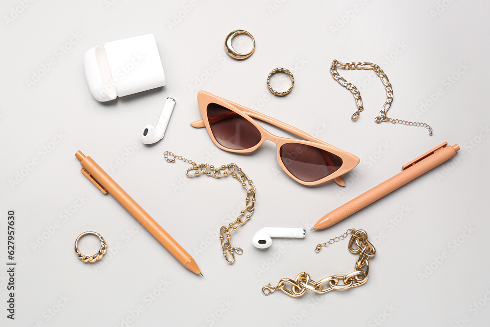 Stylish sunglasses with beautiful jewellery and earphones on grey background