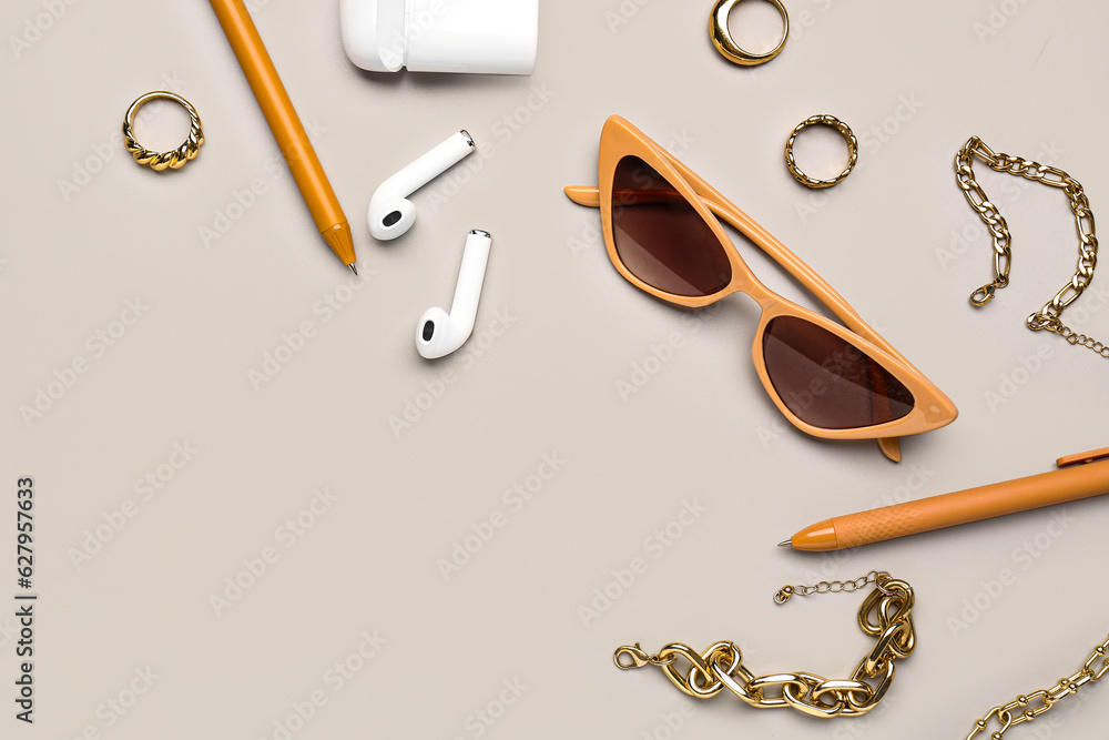 Stylish sunglasses with beautiful jewellery and earphones on grey background