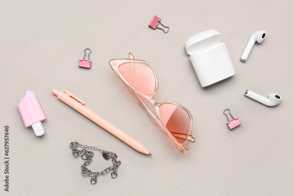 Stylish sunglasses with stationery supplies and earphones on grey background