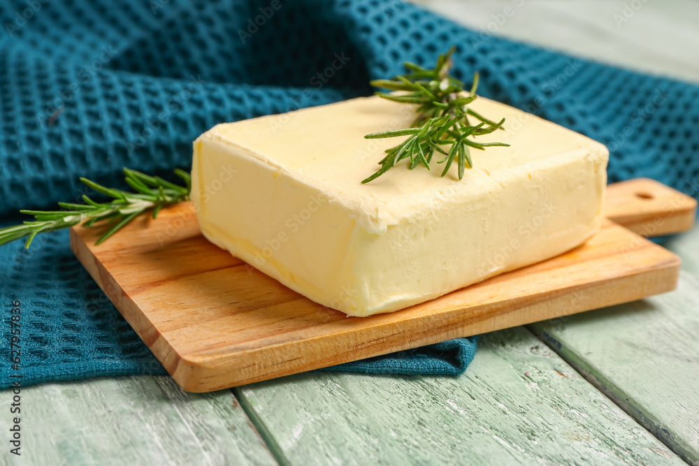 Board with fresh butter and rosemary on green wooden background