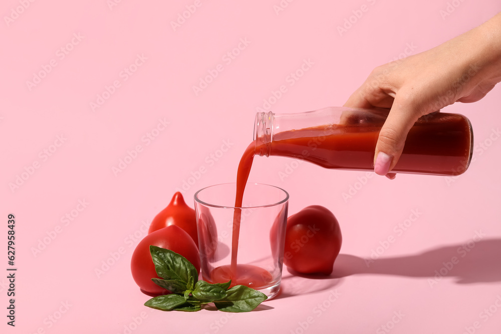 Woman pouring tasty tomato juice from bottle into glass on pink background