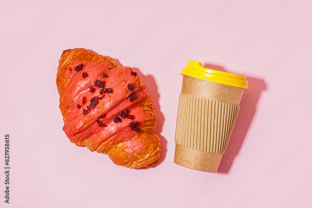 Sweet croissant and paper cup of coffee on pink table