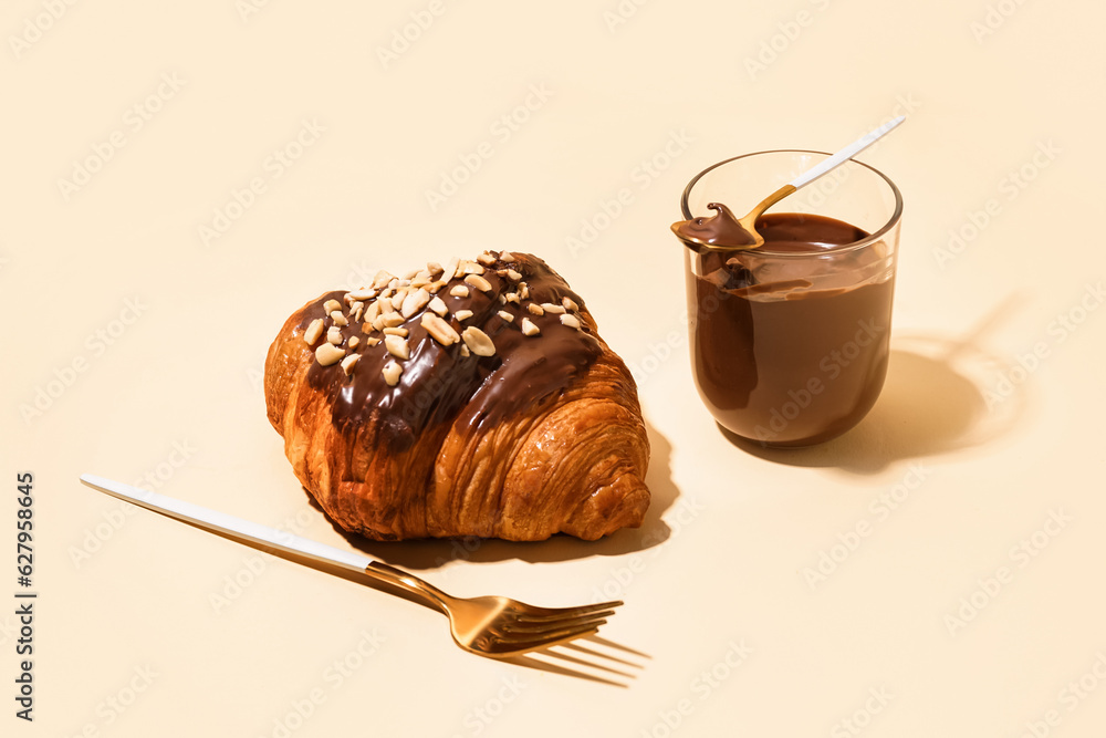 Sweet croissant and glass of chocolate on beige background