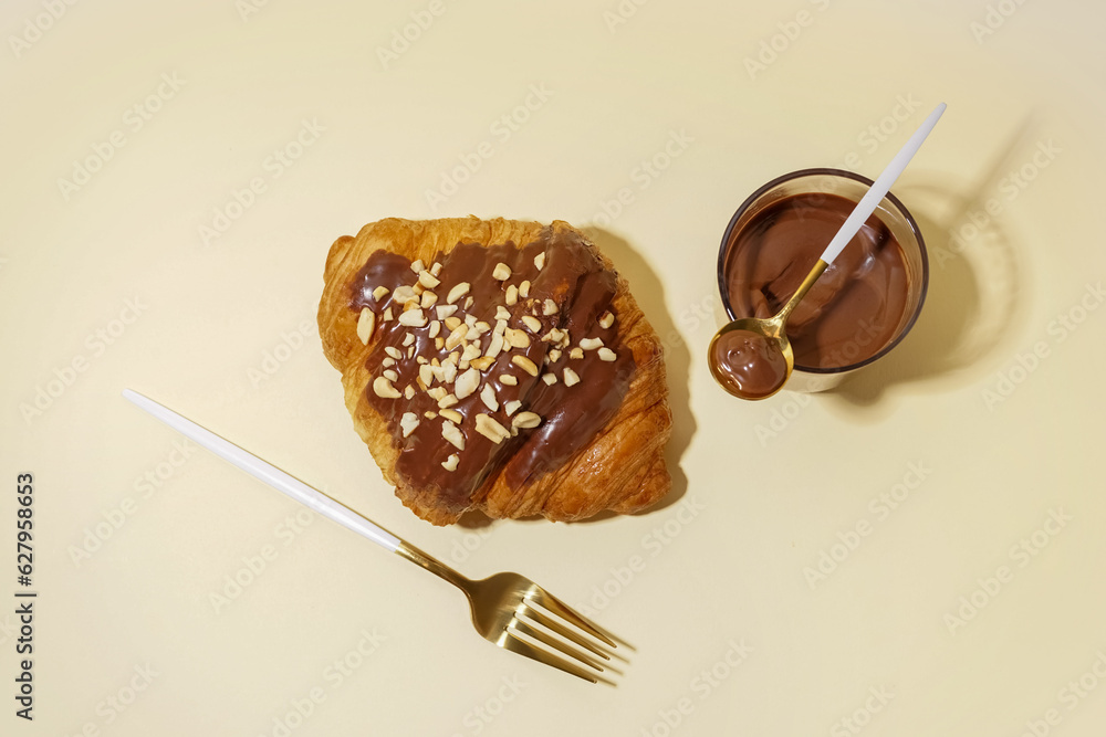 Sweet croissant and glass of chocolate on beige background