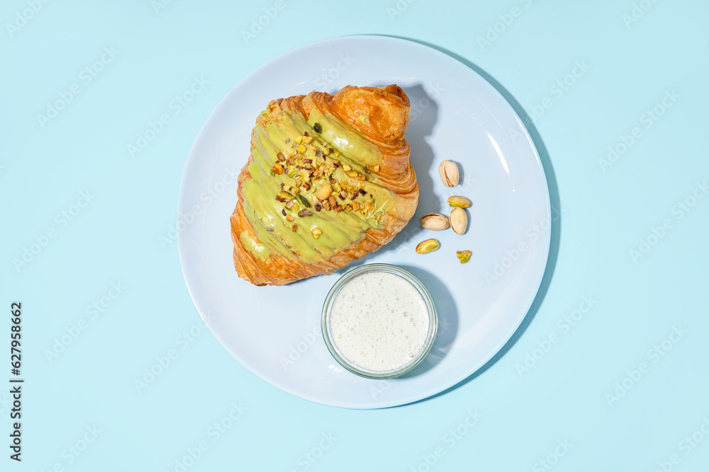 Plate with sweet croissant and pistachio nuts on blue background