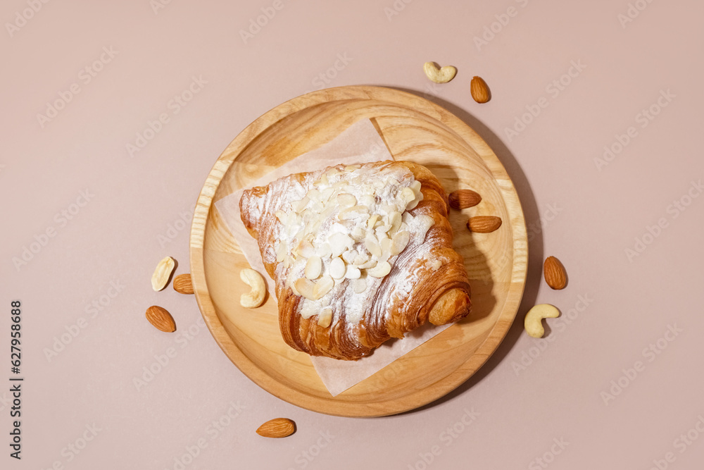 Wooden plate of sweet croissant with powdered sugar and different nuts on pink background