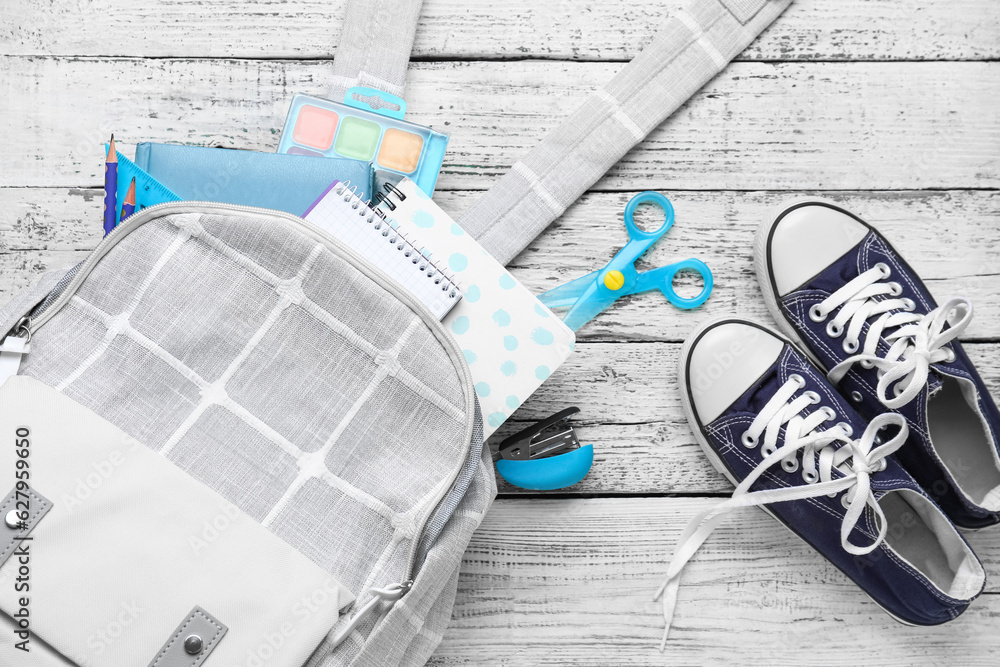 Grey school backpack with notebooks, watercolors and sneakers on white wooden background