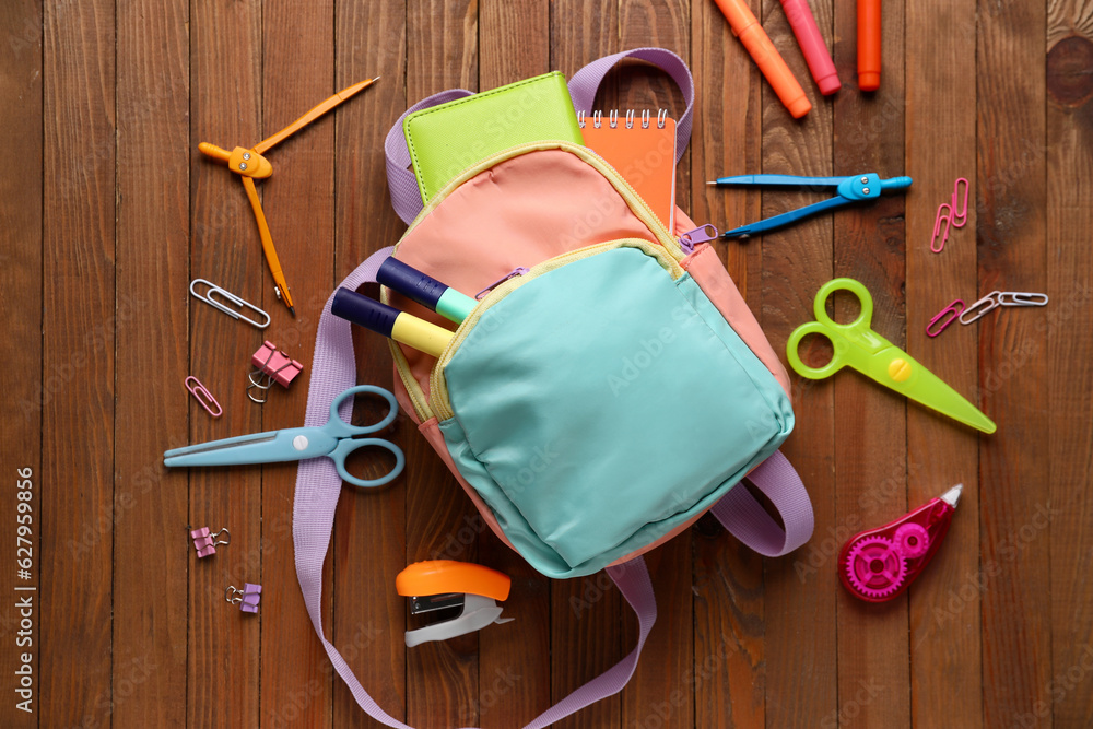 Colorful school backpack with different stationery on wooden background