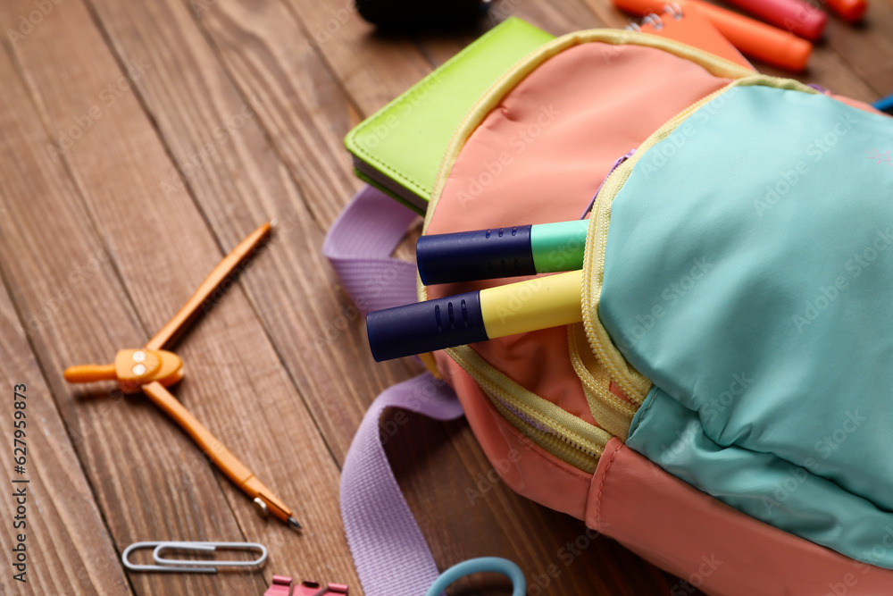 Colorful school backpack with different stationery on wooden background