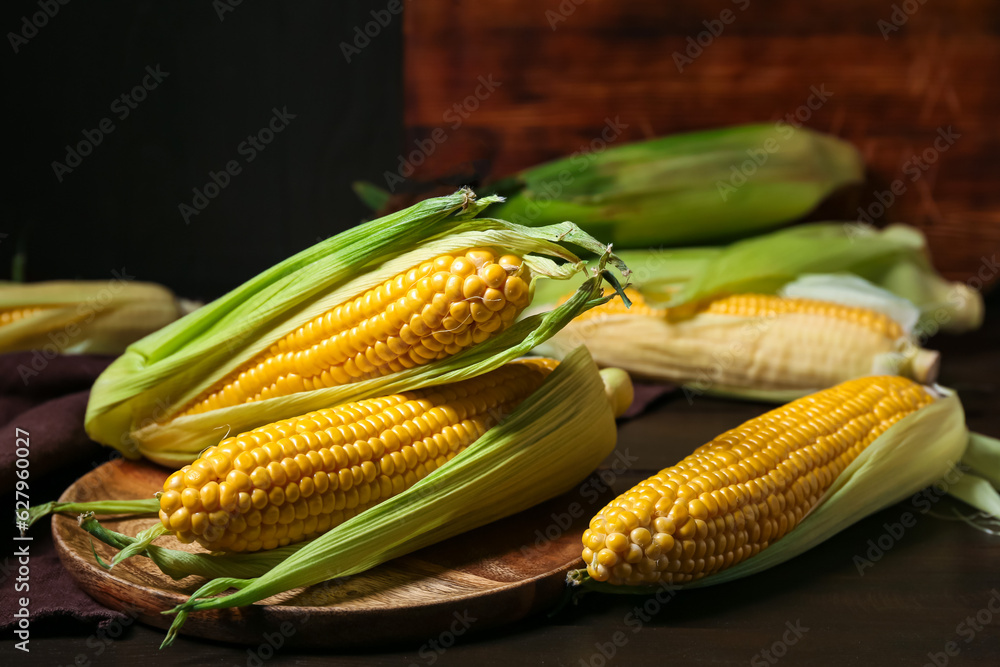 Plate with fresh corn cobs on black wooden table