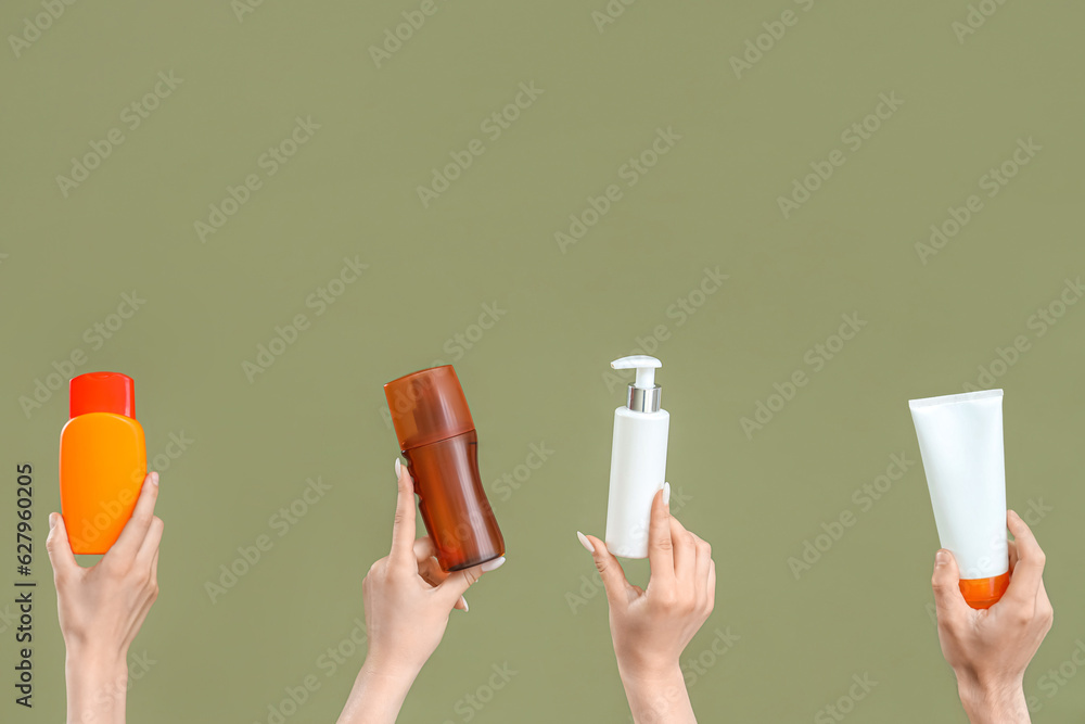 Female hands with bottles of sunscreen cream on green background