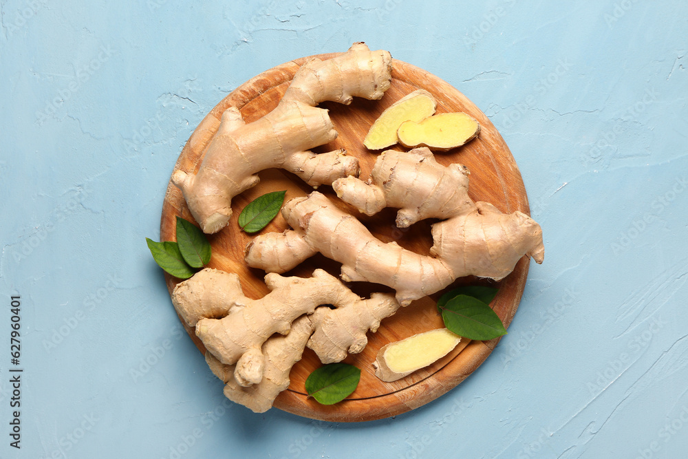 Wooden board with fresh ginger roots and leaves on blue background