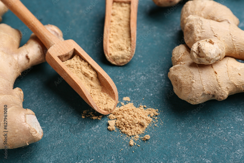 Fresh ginger roots and wooden scoops with dried powder on blue background