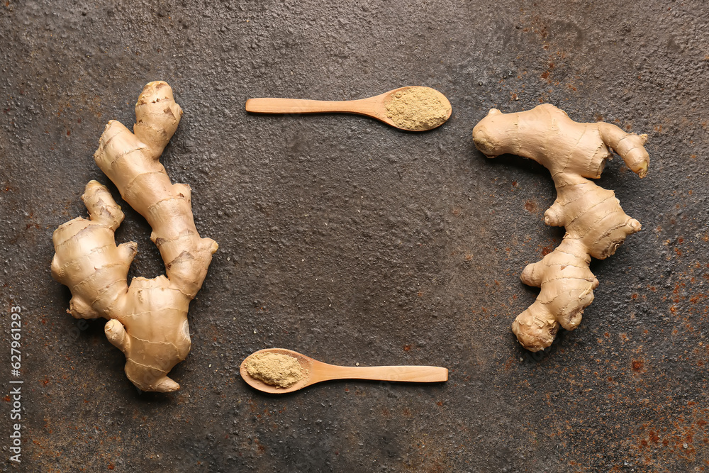 Frame made of fresh ginger roots and wooden spoons with dried powder on dark background