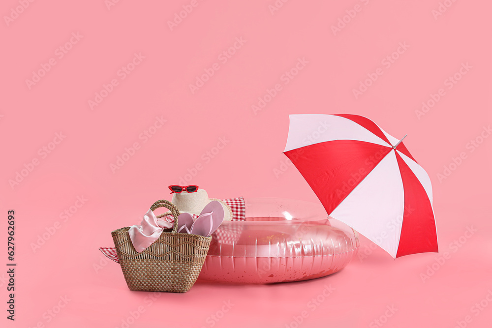 Beach accessories with bag, swim ring and umbrella on pink background