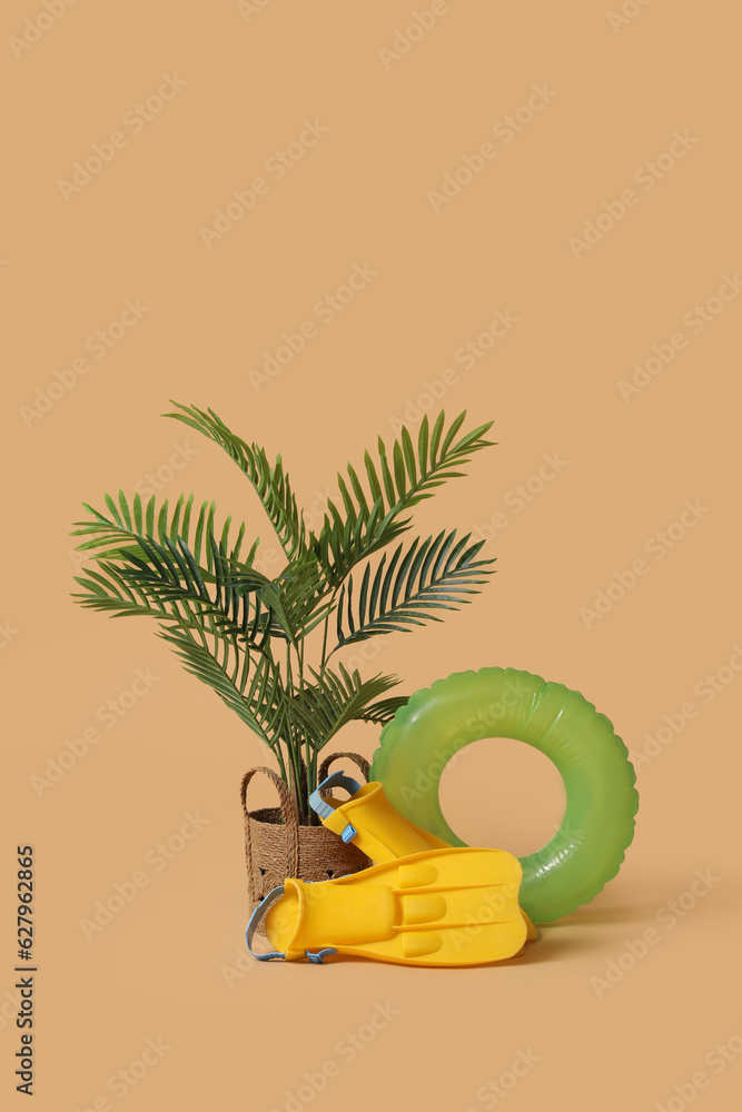 Swim ring with flippers and palm tree on beige background