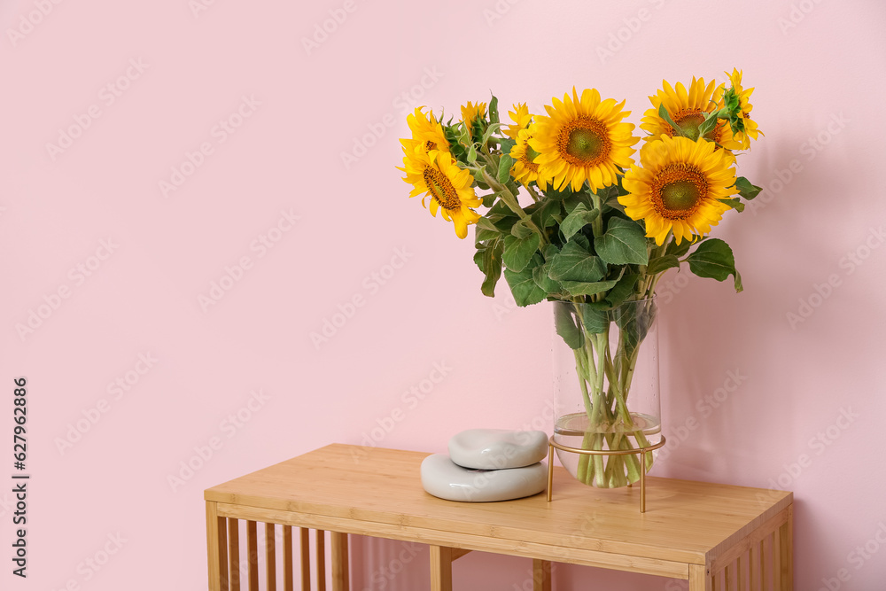 Vase with beautiful sunflowers and stones on table near pink wall in room