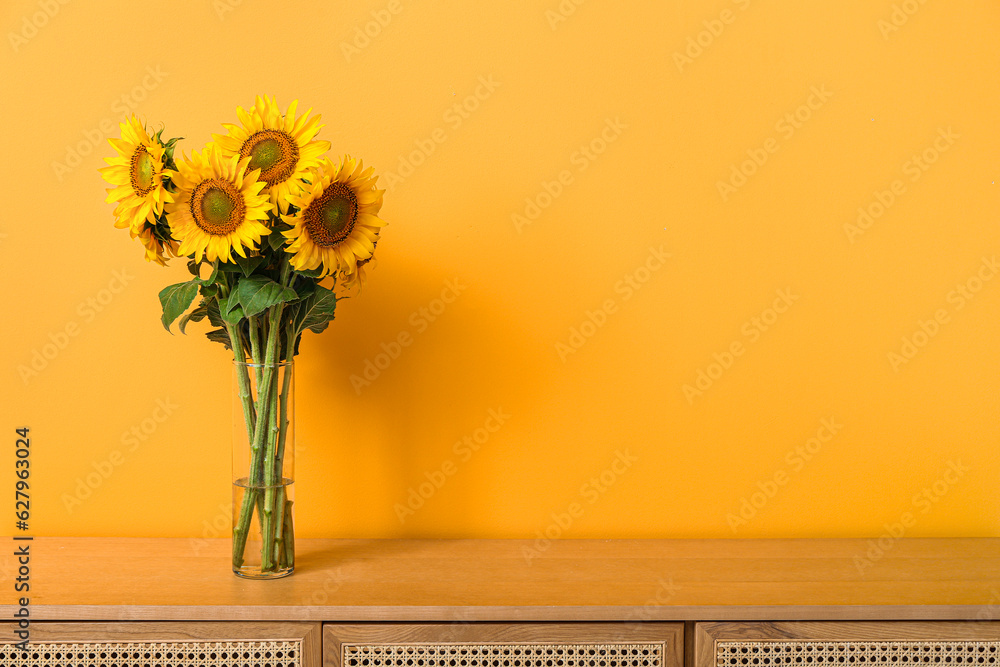 Vase with beautiful sunflowers on table near orange wall in room