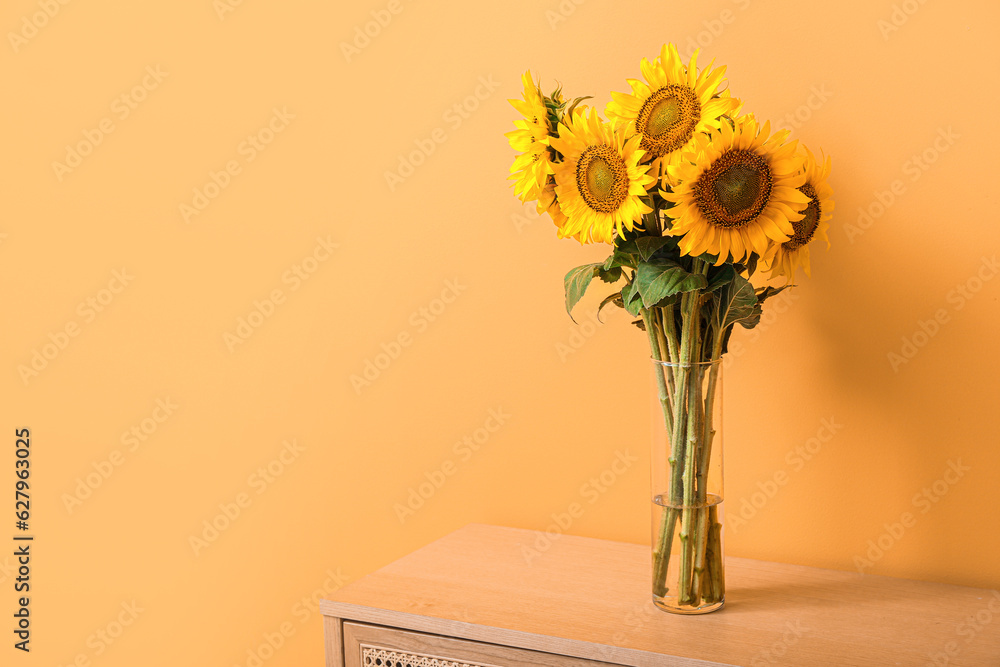 Vase with beautiful sunflowers on table near orange wall in room