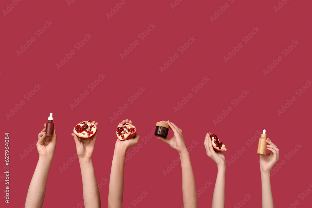 Female hands holding cosmetic products and pomegranate on red background