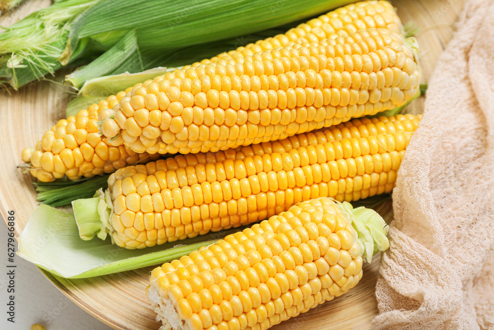 Wooden plate with fresh corn cobs, closeup