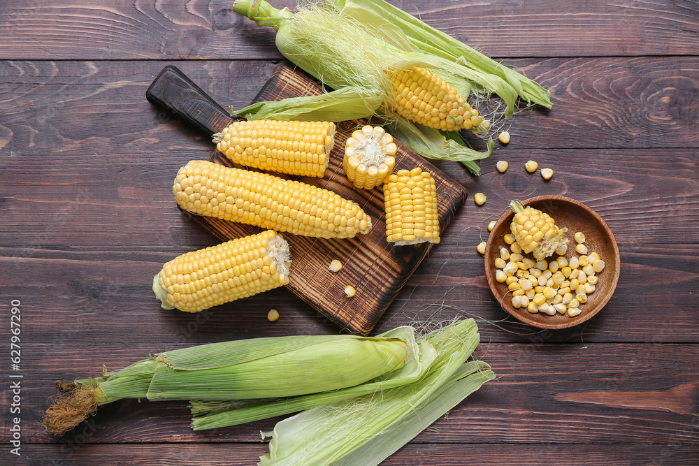 Board with fresh corn cobs on dark wooden table