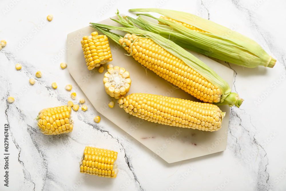 Board with fresh corn cobs on white marble table