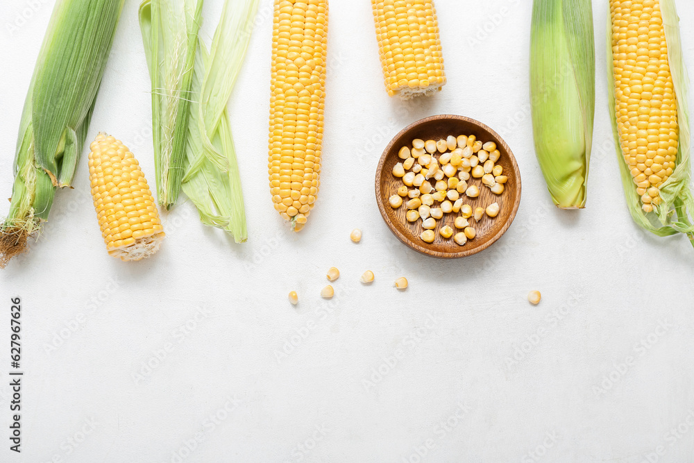 Fresh corn cobs and wooden bowl with kernels on white table