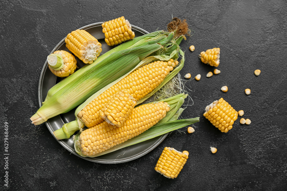 Plate with fresh corn cobs on black table