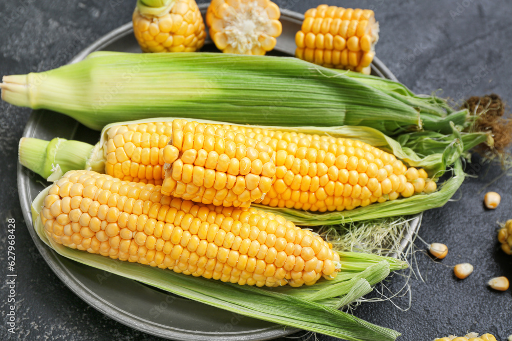 Plate with fresh corn cobs on black table, closeup